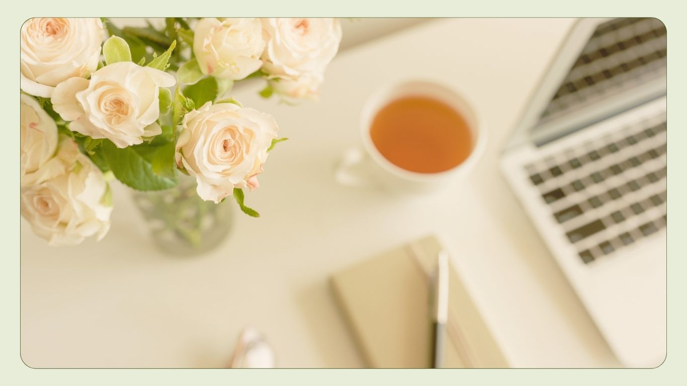 Soft arrangement of roses, a cup of tea, and a notebook on a light surface